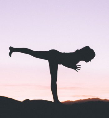 A silhouette of a fit woman practicing yoga on a high cliff at sunset